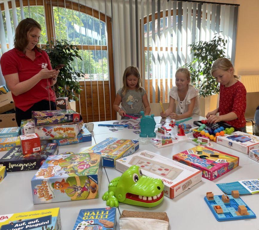 Erwachsene und drei Mädchen hinter einem Tisch mit Spielen