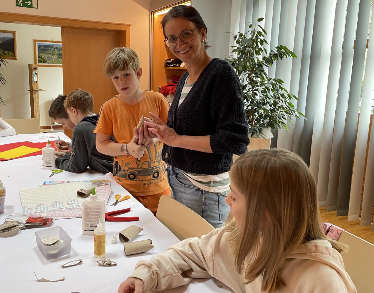 Kinder und eine Erwachsene beim Osterbasteln am Tisch, dahinter Bücherregale