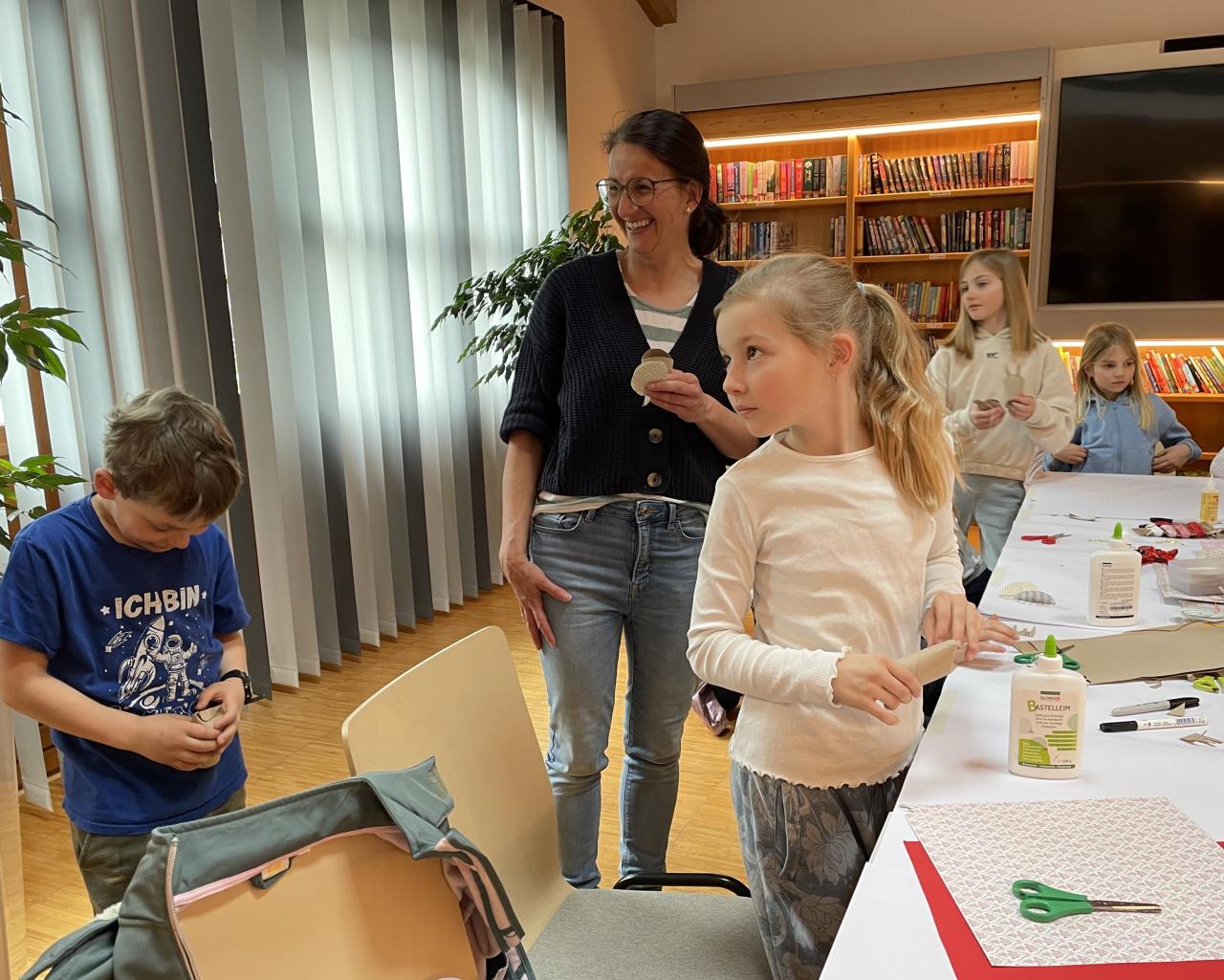 Kinder beim Osterbasteln am Tisch, dahinter Bücherregale