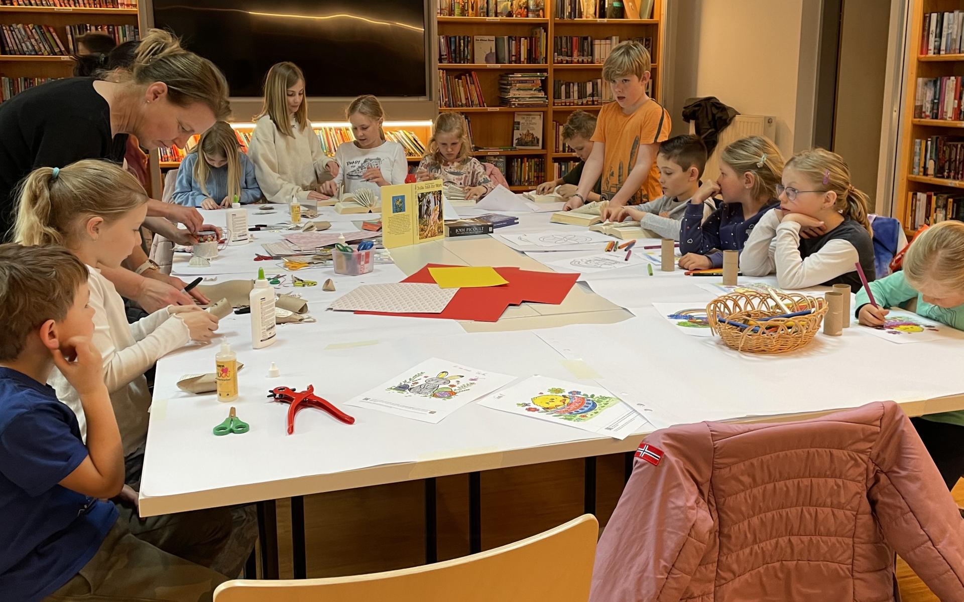 Kinder und eine Erwachsene beim Osterbasteln am Tisch, dahinter Bücherregale