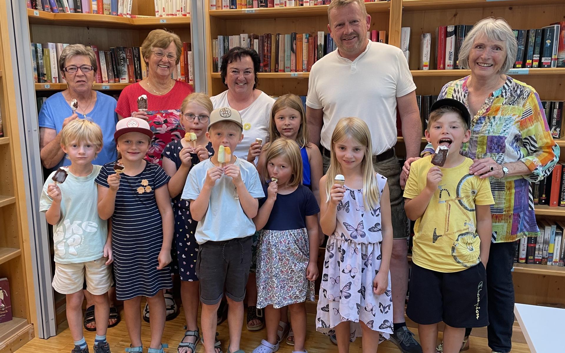 Kinder in der Bücherei stehend und ein Eis schleckend. Dahinter Erwachsene und Bücherregale