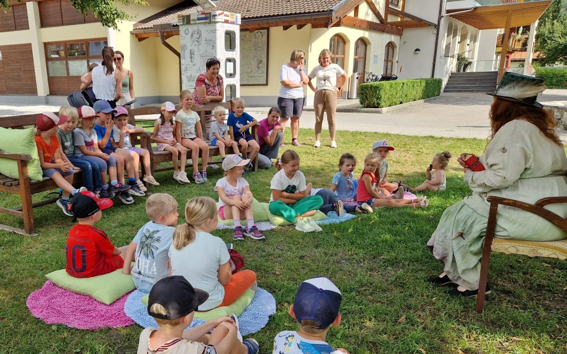 Kinder und Märchenerzählerin auf Decken und auf Sesseln sitzend