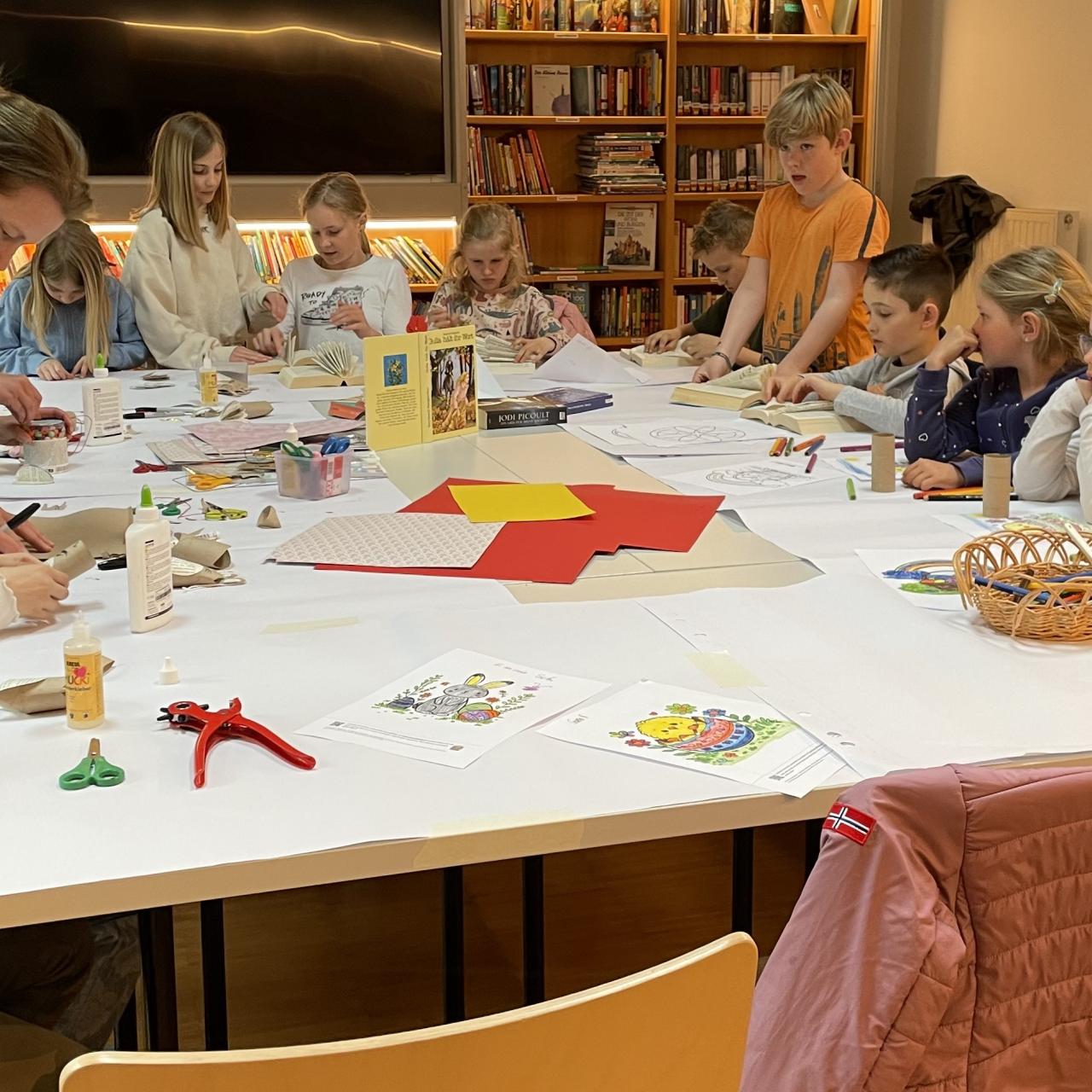 Kinder und eine Erwachsene beim Osterbasteln am Tisch, dahinter Bücherregale