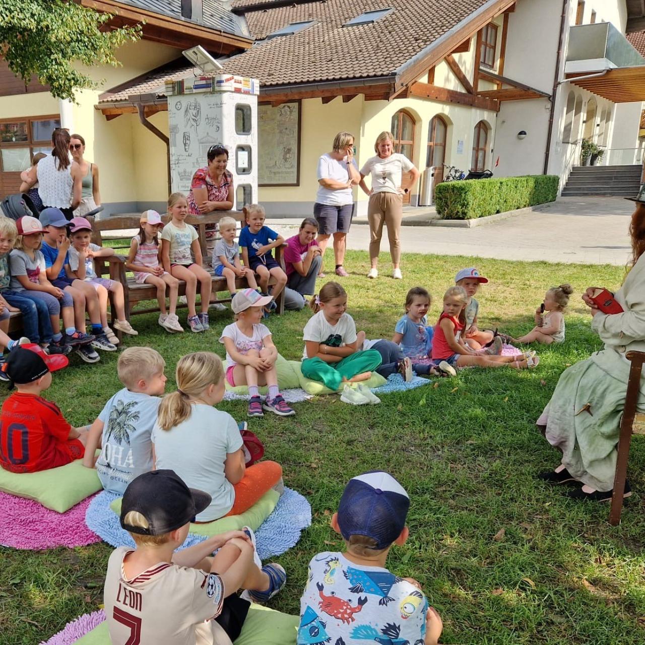 Kinder und Märchenerzählerin auf Decken und auf Sesseln sitzend